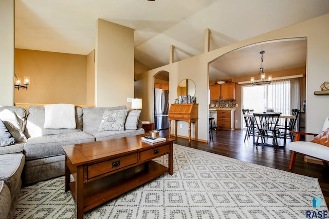 living room featuring arched walkways, lofted ceiling, an inviting chandelier, and wood finished floors