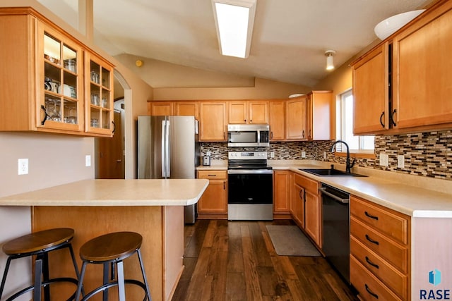 kitchen with a kitchen bar, dark wood-type flooring, stainless steel appliances, a peninsula, and vaulted ceiling