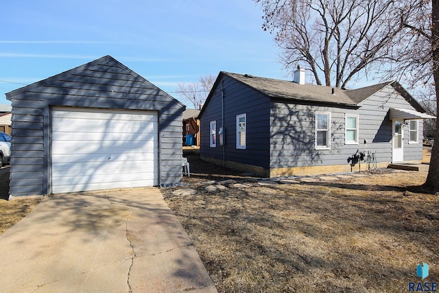 exterior space featuring a detached garage, an outbuilding, a chimney, and driveway