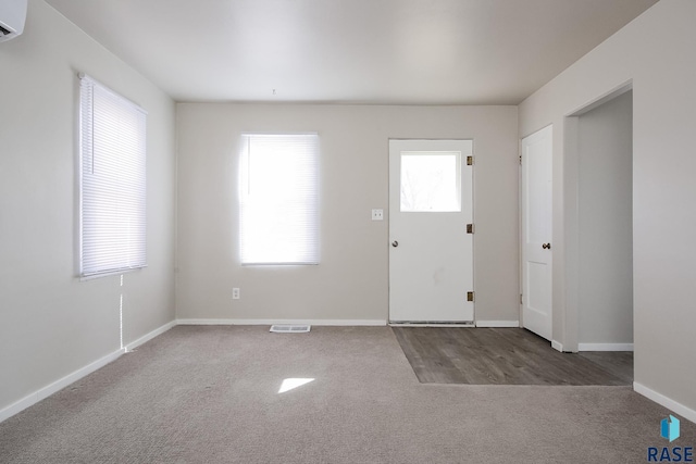 carpeted foyer with baseboards, visible vents, and a wall mounted air conditioner