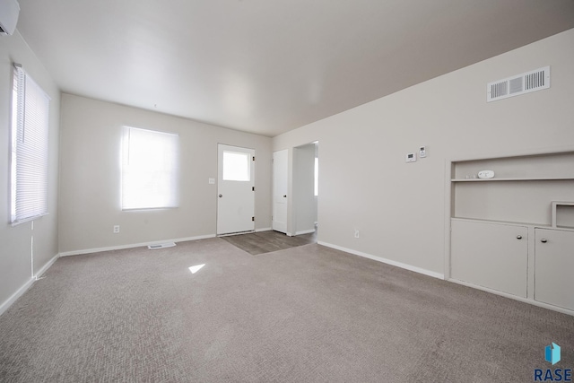 unfurnished living room with visible vents, baseboards, carpet, and an AC wall unit