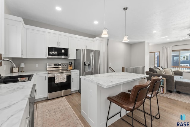 kitchen with a sink, light wood-style floors, appliances with stainless steel finishes, a kitchen bar, and open floor plan