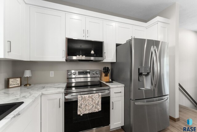 kitchen with light stone countertops, stainless steel appliances, light wood-style floors, white cabinetry, and a sink