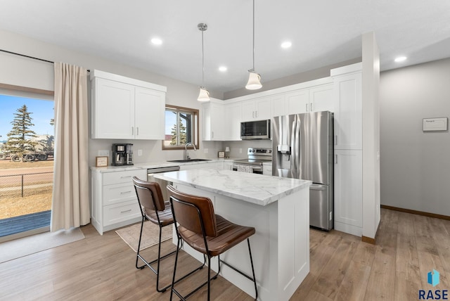 kitchen with appliances with stainless steel finishes, a kitchen island, light wood-style floors, and a sink