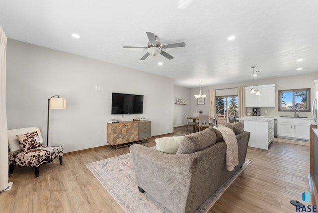 living room with light wood finished floors, recessed lighting, ceiling fan with notable chandelier, and baseboards