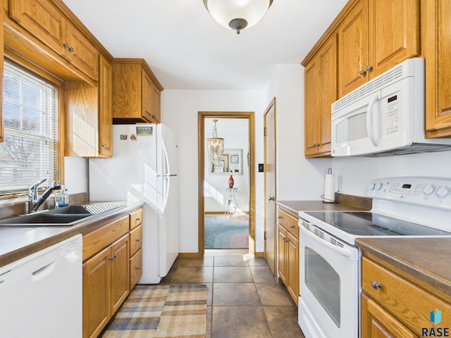 kitchen with brown cabinetry, white appliances, dark tile patterned flooring, and a sink