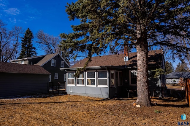 rear view of house featuring fence, a chimney, a sunroom, and roof with shingles