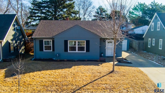 bungalow with concrete driveway, a chimney, roof with shingles, and fence