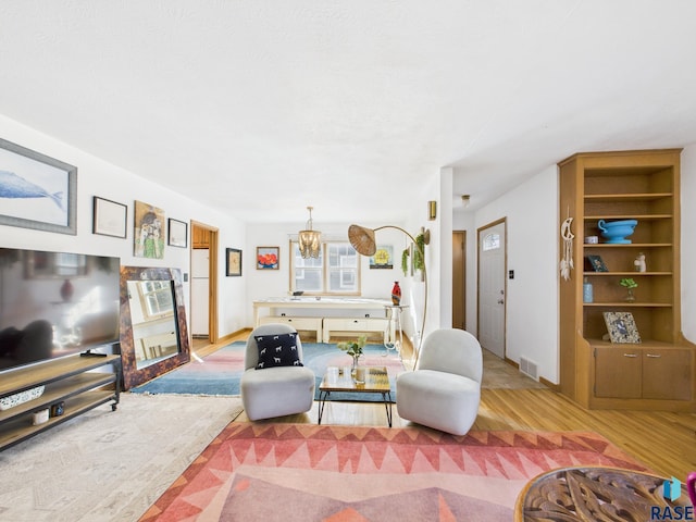 living room with a notable chandelier, light wood-style floors, and visible vents