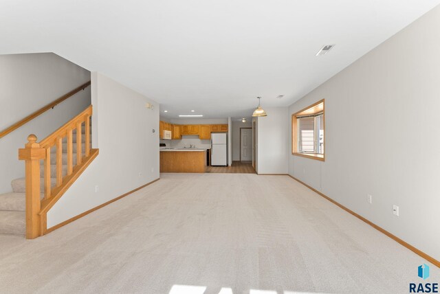 unfurnished living room featuring stairs, baseboards, and light carpet