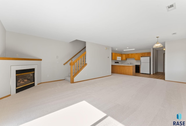 unfurnished living room featuring baseboards, light colored carpet, stairs, and a tile fireplace