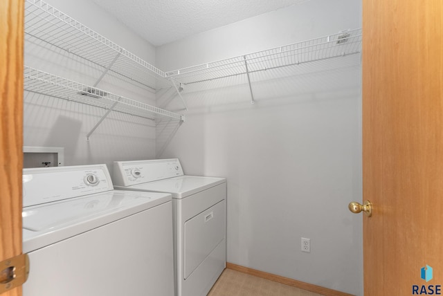 washroom featuring washer and clothes dryer, laundry area, a textured ceiling, and baseboards