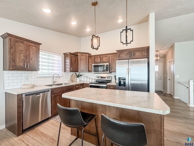 kitchen with light wood-type flooring, a sink, a kitchen island, backsplash, and appliances with stainless steel finishes