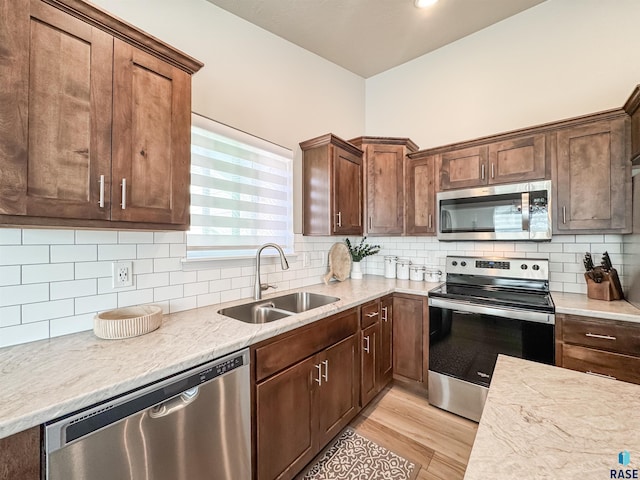 kitchen with light wood-style flooring, a sink, light countertops, appliances with stainless steel finishes, and tasteful backsplash