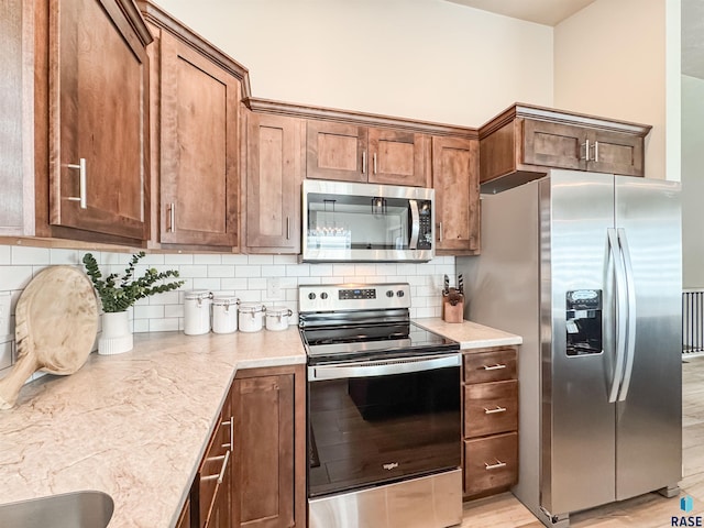 kitchen with light stone counters, brown cabinetry, stainless steel appliances, decorative backsplash, and light wood-style floors