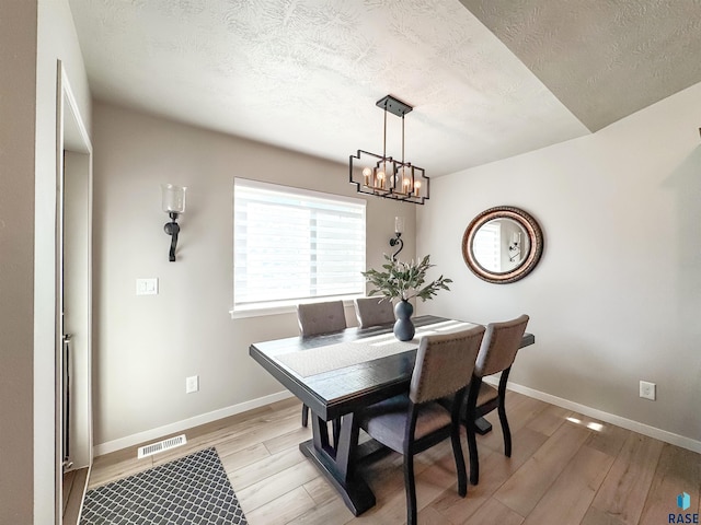 dining room featuring visible vents, baseboards, light wood-style floors, a notable chandelier, and a textured ceiling