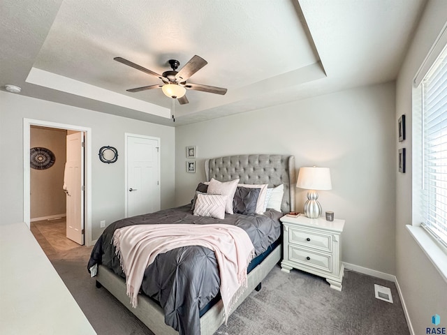 carpeted bedroom with visible vents, a ceiling fan, a textured ceiling, baseboards, and a raised ceiling