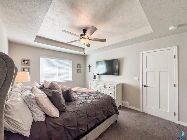 carpeted bedroom featuring a textured ceiling, a raised ceiling, and baseboards