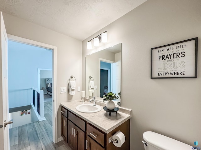 half bathroom featuring a textured ceiling, toilet, vanity, and wood finished floors