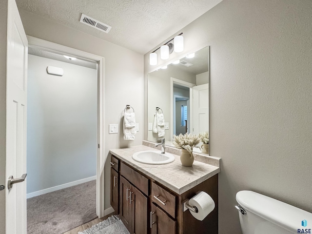 half bath with visible vents, baseboards, toilet, vanity, and a textured ceiling