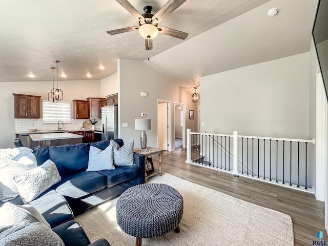 living area with ceiling fan with notable chandelier, light wood-type flooring, and lofted ceiling