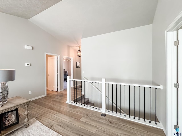 hallway with wood finished floors, baseboards, an inviting chandelier, vaulted ceiling, and an upstairs landing