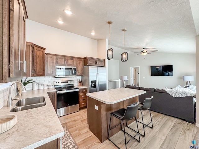 kitchen with light wood-style flooring, a sink, a center island, stainless steel appliances, and lofted ceiling