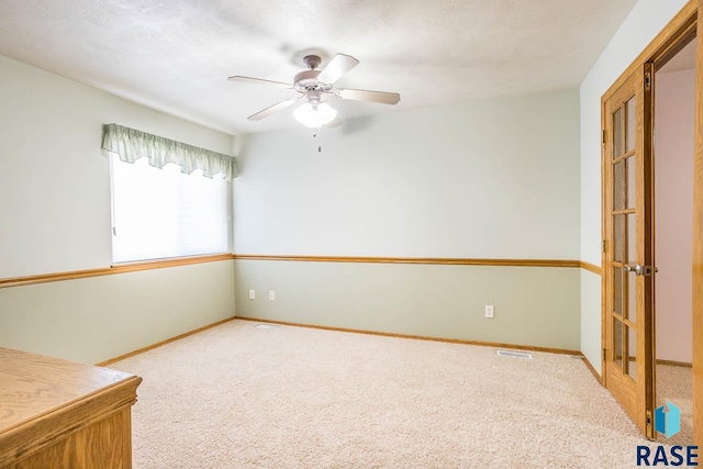 carpeted empty room with a ceiling fan, baseboards, visible vents, and a textured ceiling