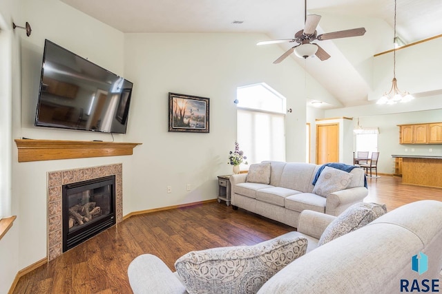 living area with high vaulted ceiling, wood finished floors, baseboards, and a tile fireplace