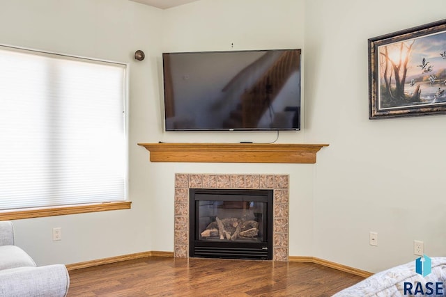 living room with a wealth of natural light, baseboards, wood finished floors, and a tile fireplace