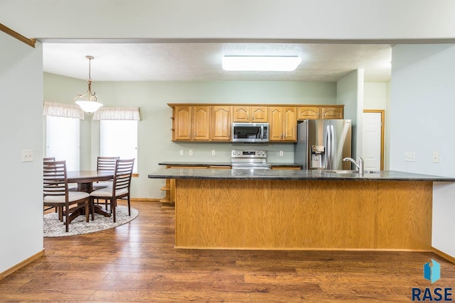 kitchen with baseboards, dark wood finished floors, a sink, appliances with stainless steel finishes, and decorative light fixtures