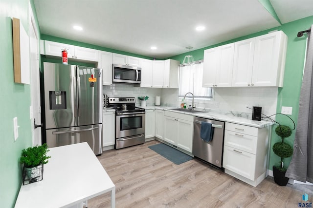 kitchen featuring light wood-type flooring, a sink, white cabinetry, appliances with stainless steel finishes, and decorative backsplash