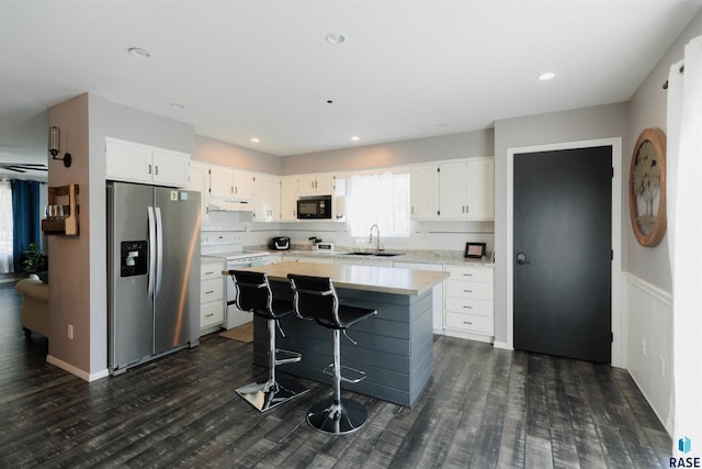 kitchen featuring black microwave, stainless steel fridge with ice dispenser, under cabinet range hood, electric stove, and a sink