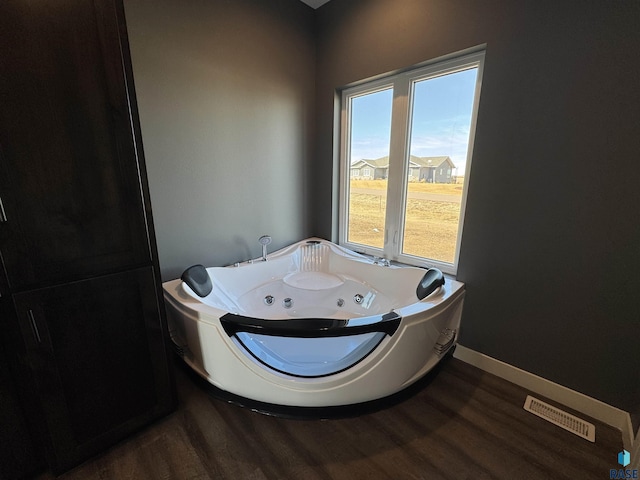 bathroom with a jetted tub, wood finished floors, visible vents, and baseboards