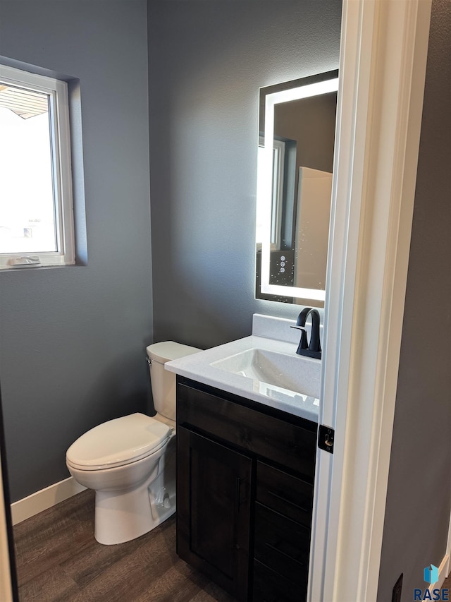 half bath featuring vanity, toilet, wood finished floors, and baseboards