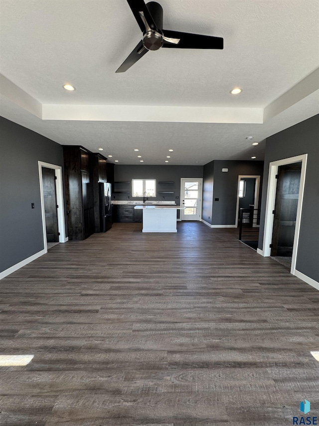 unfurnished living room with dark wood finished floors, a ceiling fan, baseboards, and a sink