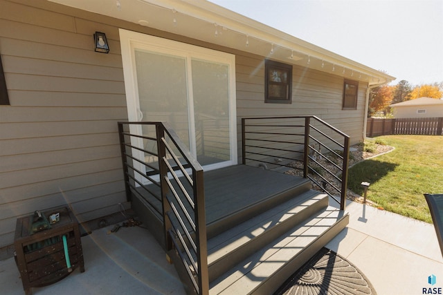 view of exterior entry with fence and a lawn