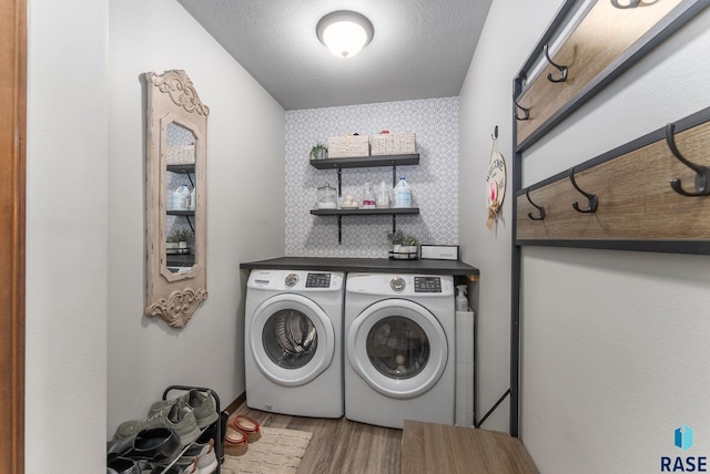 washroom featuring an accent wall, washing machine and dryer, laundry area, wood finished floors, and a textured ceiling