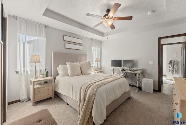 bedroom with a tray ceiling, light colored carpet, baseboards, and a textured ceiling