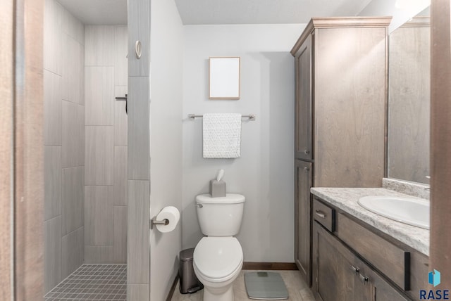 full bathroom with baseboards, toilet, vanity, and a tile shower