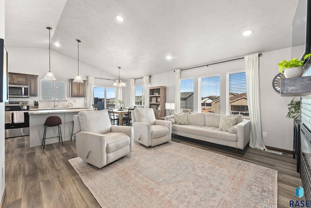 living area with a notable chandelier, a glass covered fireplace, lofted ceiling, and dark wood-style flooring