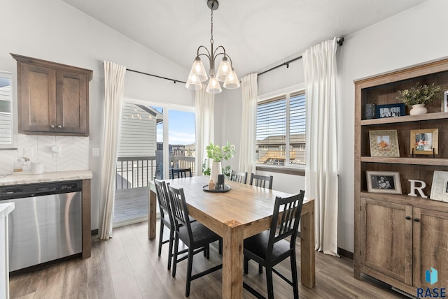 dining space with lofted ceiling, a healthy amount of sunlight, wood finished floors, and an inviting chandelier