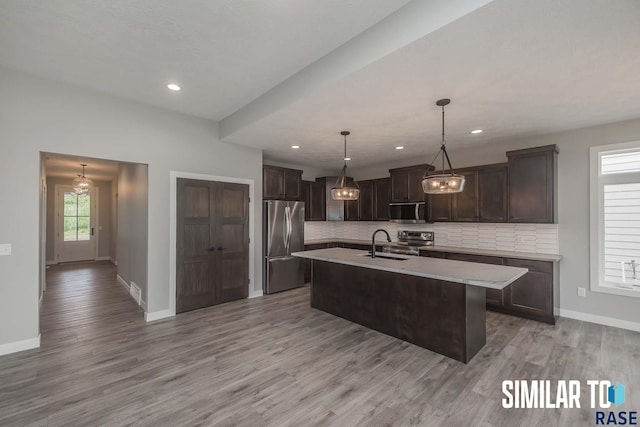 kitchen featuring an island with sink, light countertops, dark brown cabinets, appliances with stainless steel finishes, and backsplash