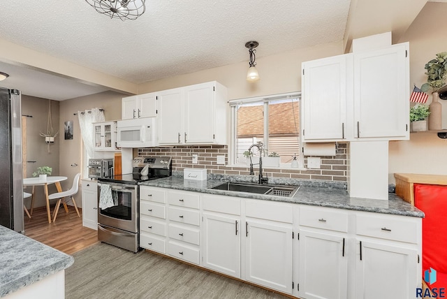 kitchen featuring light wood-style flooring, a sink, stainless steel appliances, white cabinets, and decorative backsplash