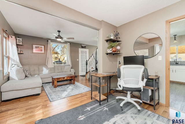 living room featuring baseboards, stairs, wood finished floors, a textured ceiling, and a ceiling fan