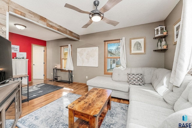 living area with wood finished floors, baseboards, beam ceiling, ceiling fan, and a textured ceiling