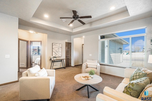 living room featuring visible vents, baseboards, a raised ceiling, and carpet