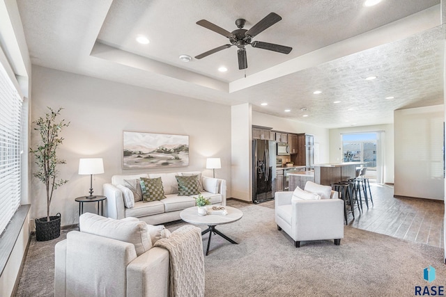 living area featuring recessed lighting, a textured ceiling, a raised ceiling, and baseboards