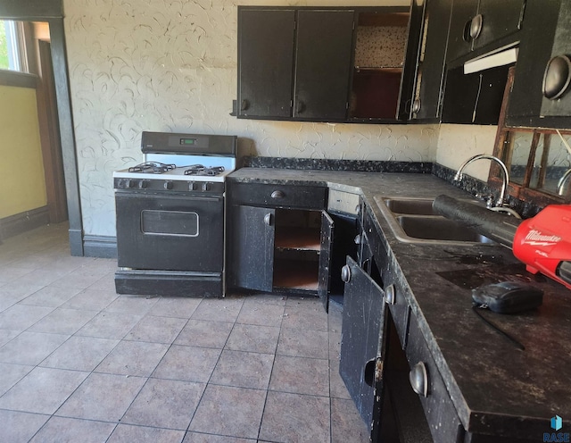 kitchen with dark countertops, open shelves, light tile patterned flooring, a sink, and gas range