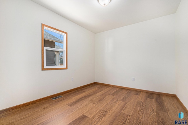 spare room featuring light wood finished floors, visible vents, and baseboards